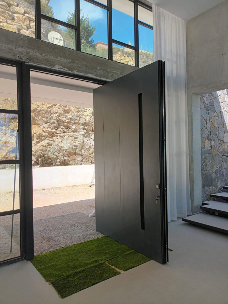 puerta-metalica-pivotante-vivienda-moderna Puerta metálica pivotante negra instalada en la entrada de una vivienda moderna